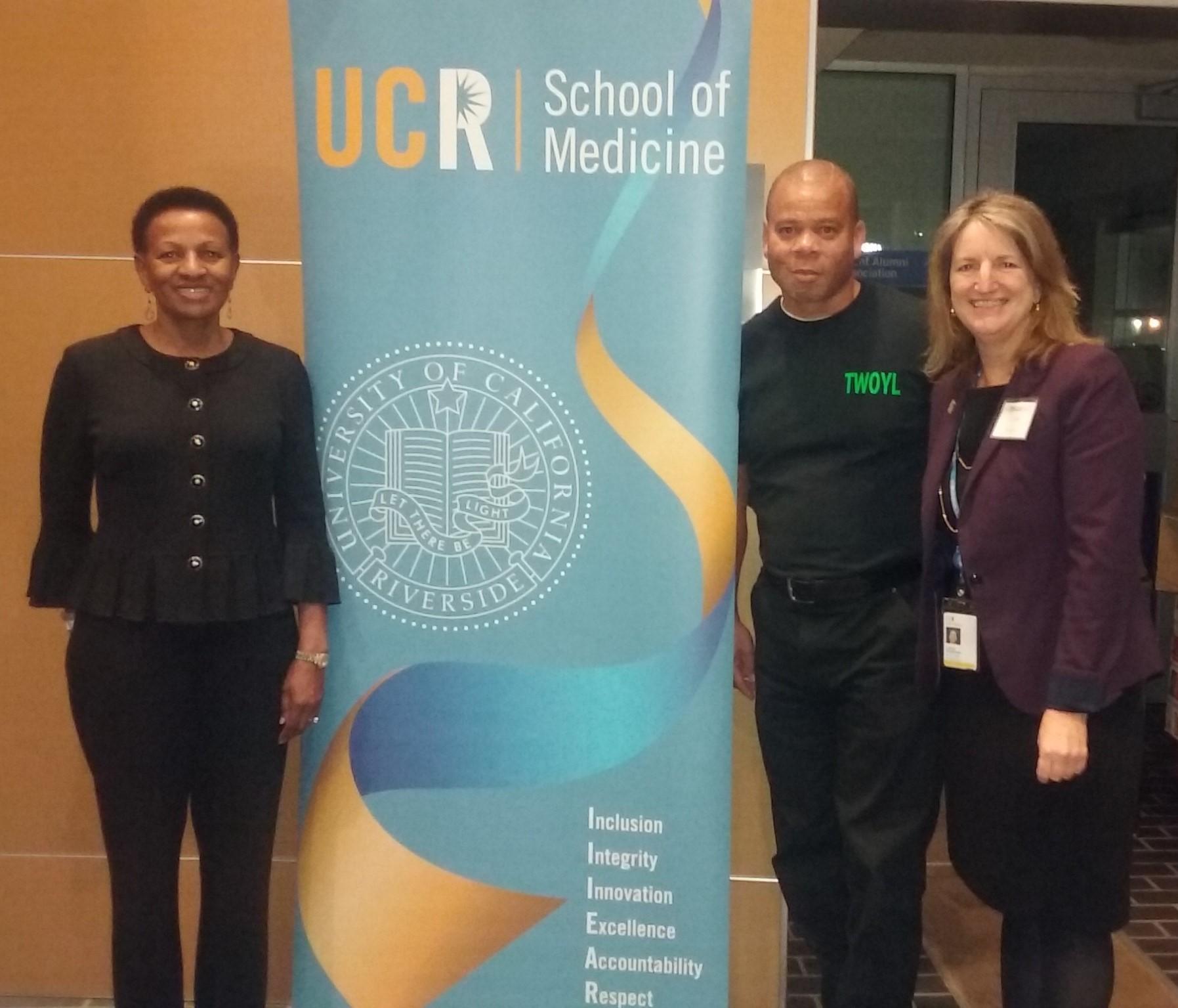 SKN member, Terry Boykins, next to University of California, Risverside School of Medicine Banner